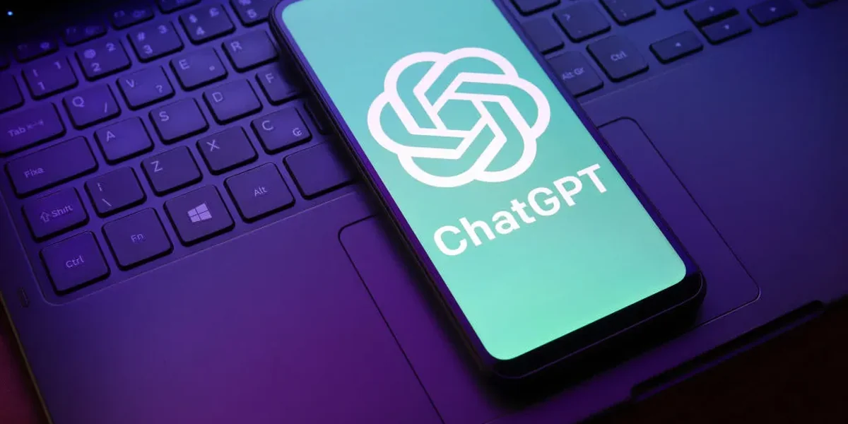 A phone resting on a laptop keyboard, showing the ChatGPT logo and name on its screen