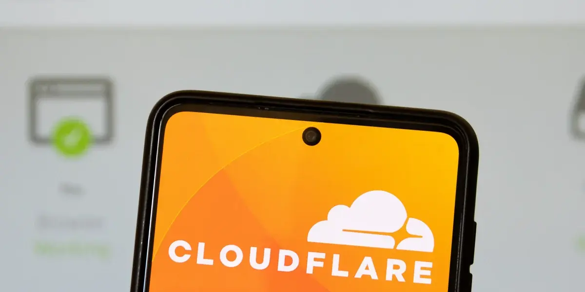 Telefono con il logo Cloudflare davanti a una pagina di stato del server, sfocata, con un segno di spunta verde