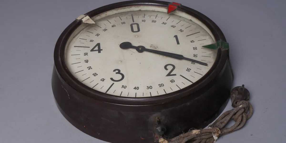 A large bakelite stopwatch-style timer lying on a grey surface, dial numbered 0 to 4 with minute markings, single black hand, cord coiled beside it