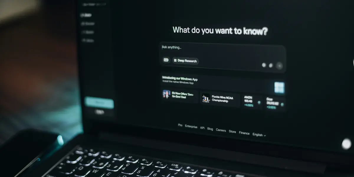 Ecranul unui laptop într-o cameră întunecată, cu interfața Perplexity deschisă pe întrebarea What do you want to know, o casetă de introducere a textului și un buton de Deep Research