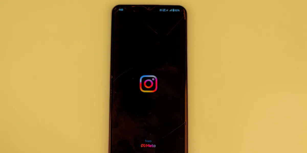 A smartphone with a black screen showing the Instagram logo, resting on a bright yellow background, with the words from Meta beneath the logo