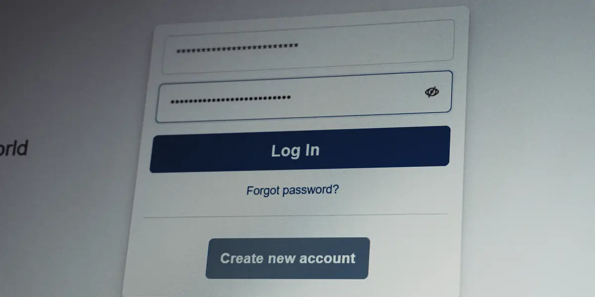 Prim-plan cu un formular de autentificare pe ecran: două câmpuri completate cu caractere ascunse prin asteriscuri și puncte, butonul albastru Log In, linkul Forgot password și butonul Create new account